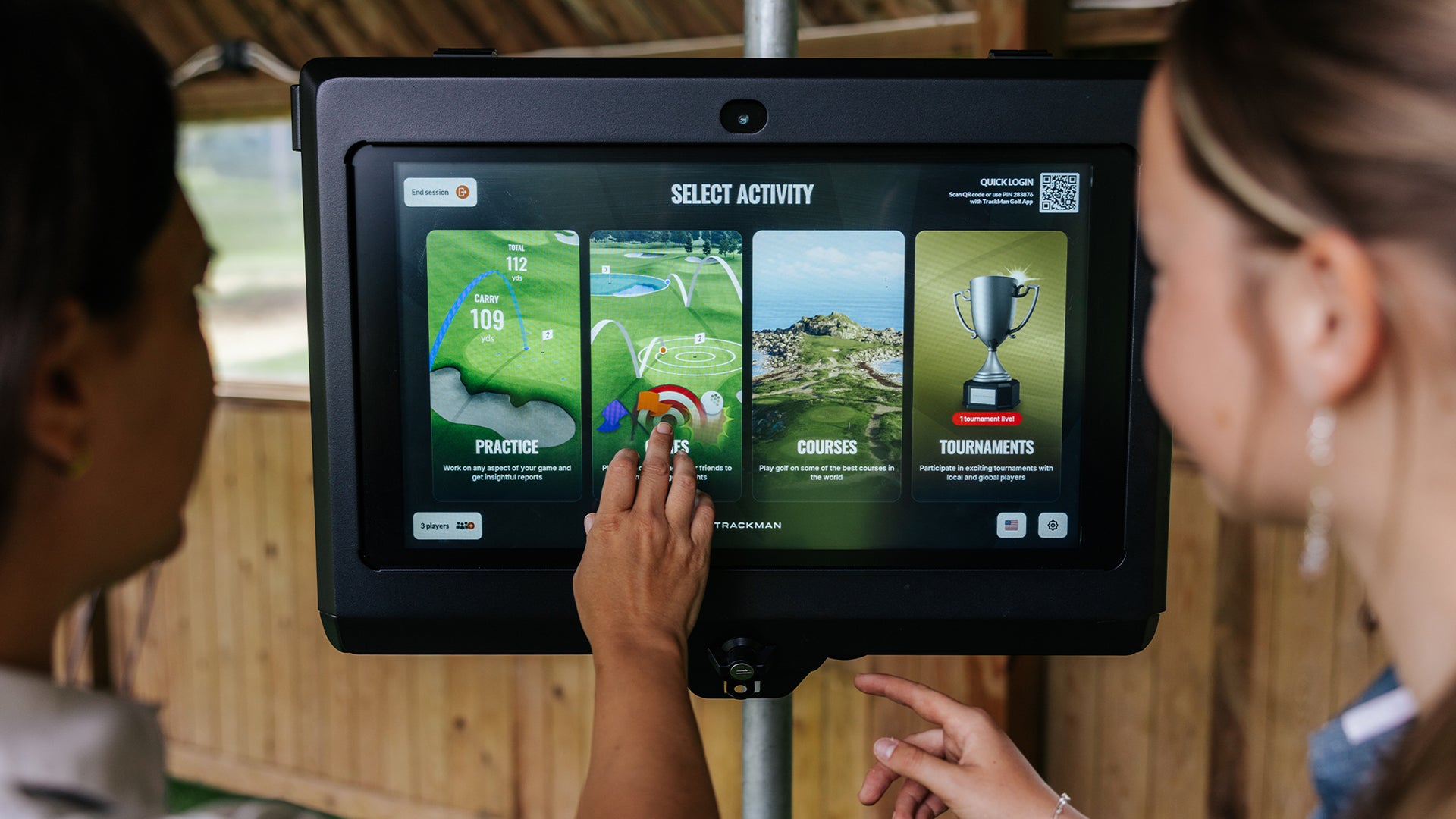 Two people interacting with Trackman touchscreen display in an indoor setting.